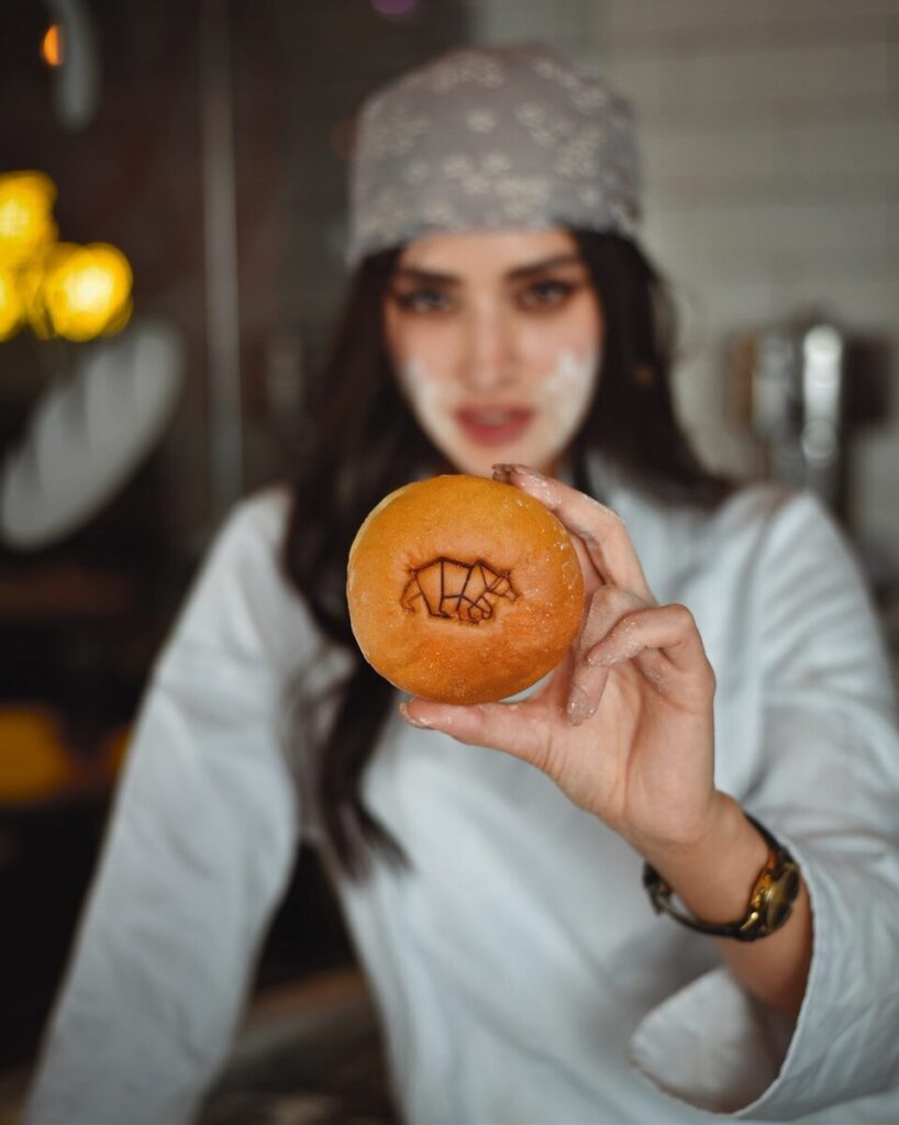 A woman holding a doughnut with a face drawn on it